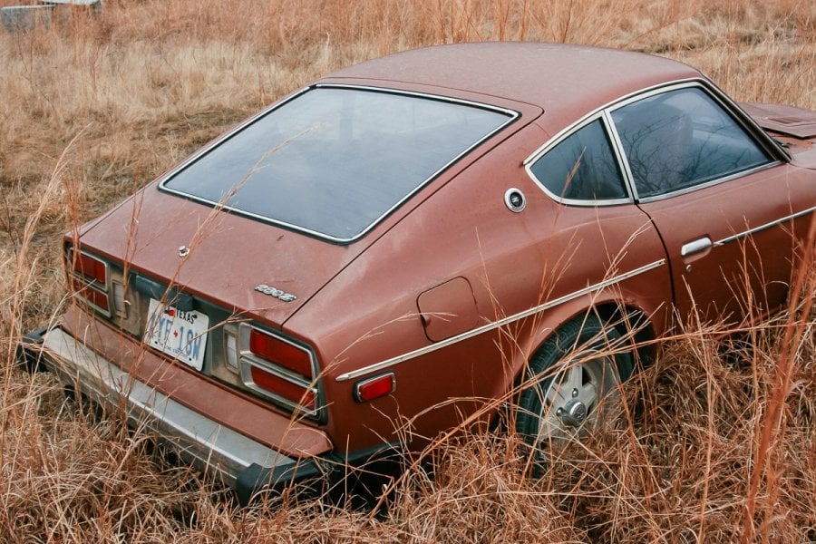 A Datsun 280z rusting at an abandoned junkyard