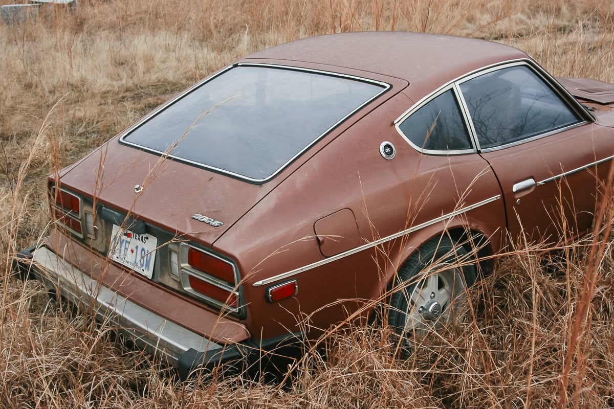 A Datsun 280z rusting at an abandoned junkyard