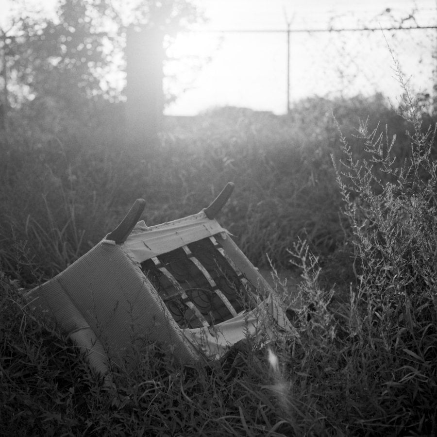 A discard chair in grass on the side of the road
