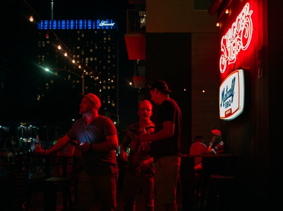Three men talking below a red neon sign at Stagger Lee bar on Rainey Street
